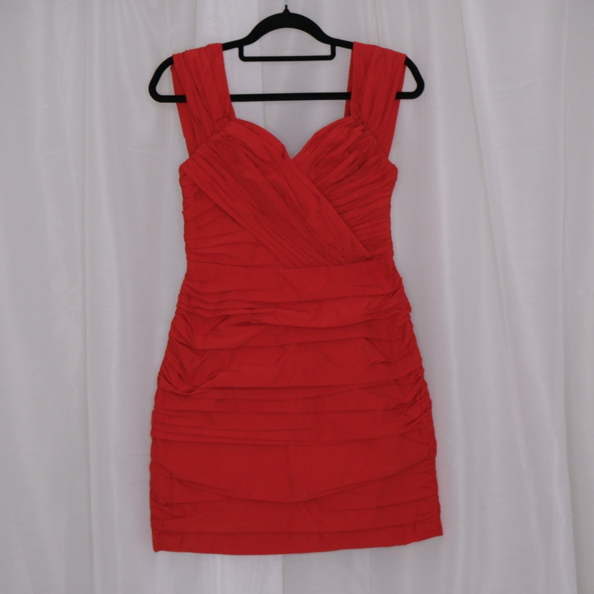 Red mini dress on a hanger against a white curtain background