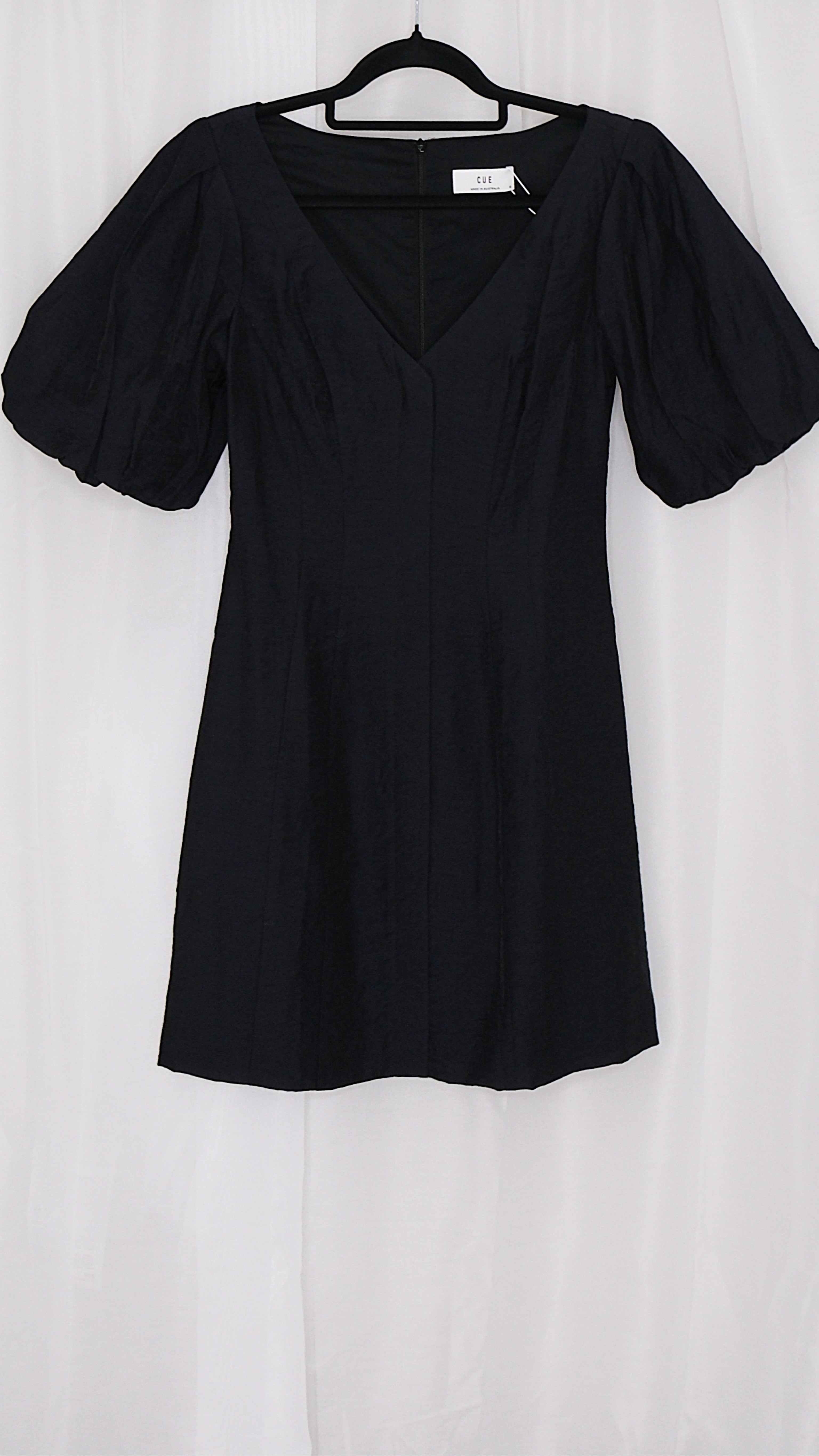 Black mini dress with puff sleeves on a hanger against a white background