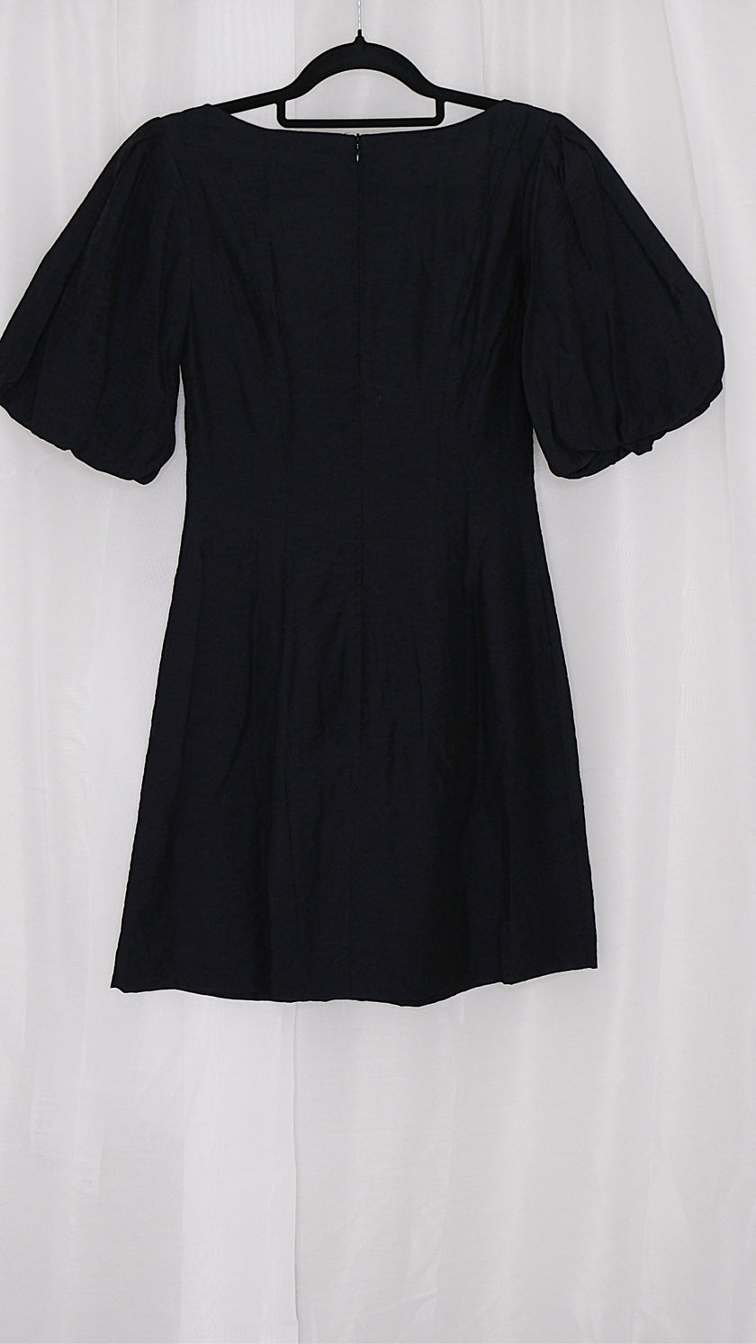 Black mini dress with puff sleeves on a hanger against a white background
