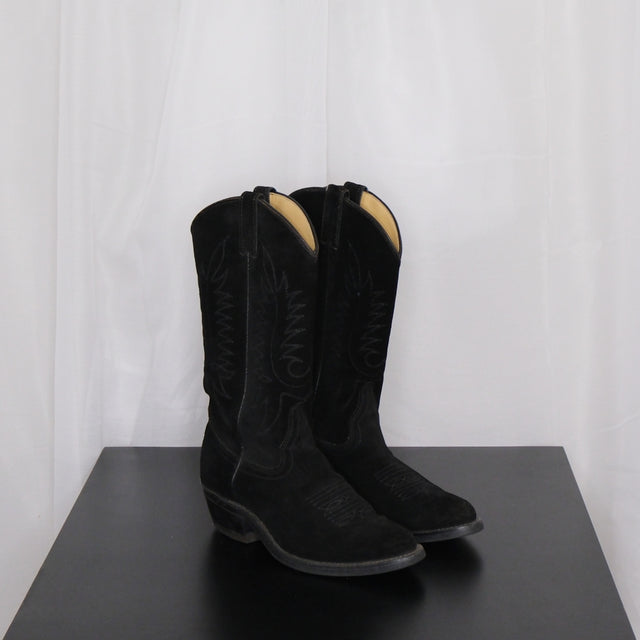 Pair of vintage black cowboy boots on a dark surface with a white curtain background