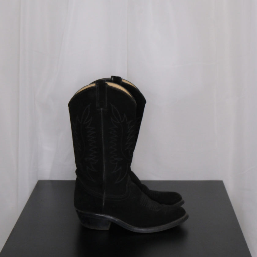 Pair of vintage black cowboy boots on a dark surface with a white curtain background