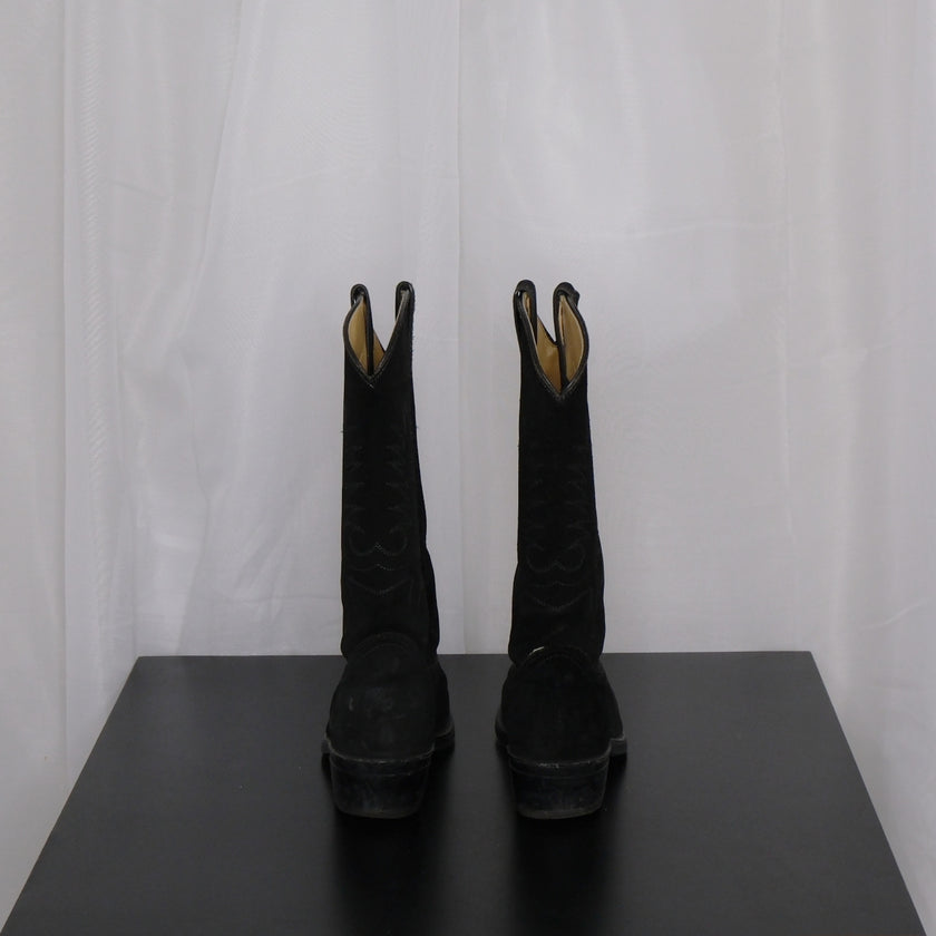 Pair of vintage black cowboy boots on a dark surface with a white curtain background