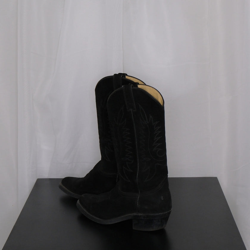 Pair of vintage black cowboy boots on a dark surface with a white curtain background