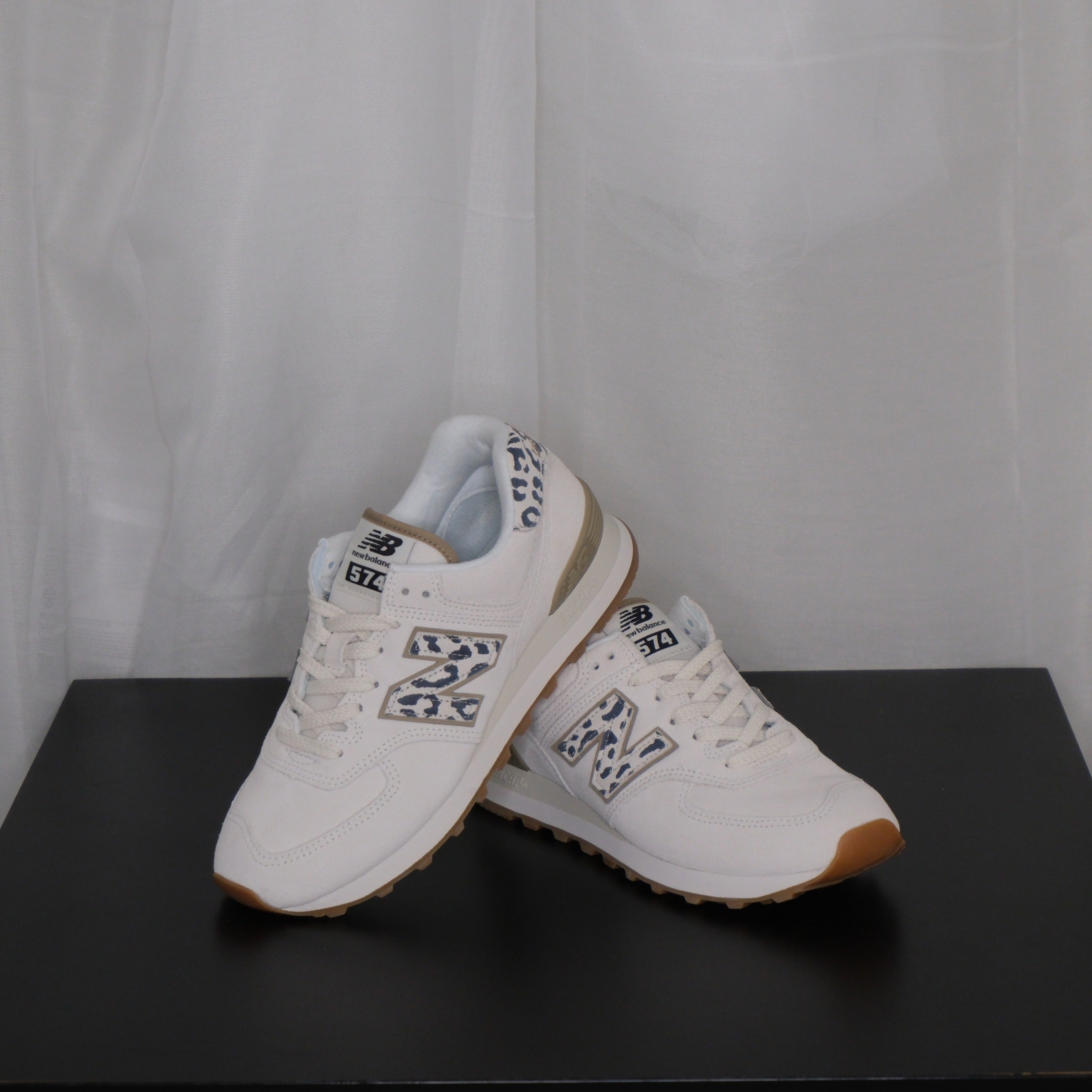 White sneakers with grey leopard design on a black surface and white sheer curtain background

