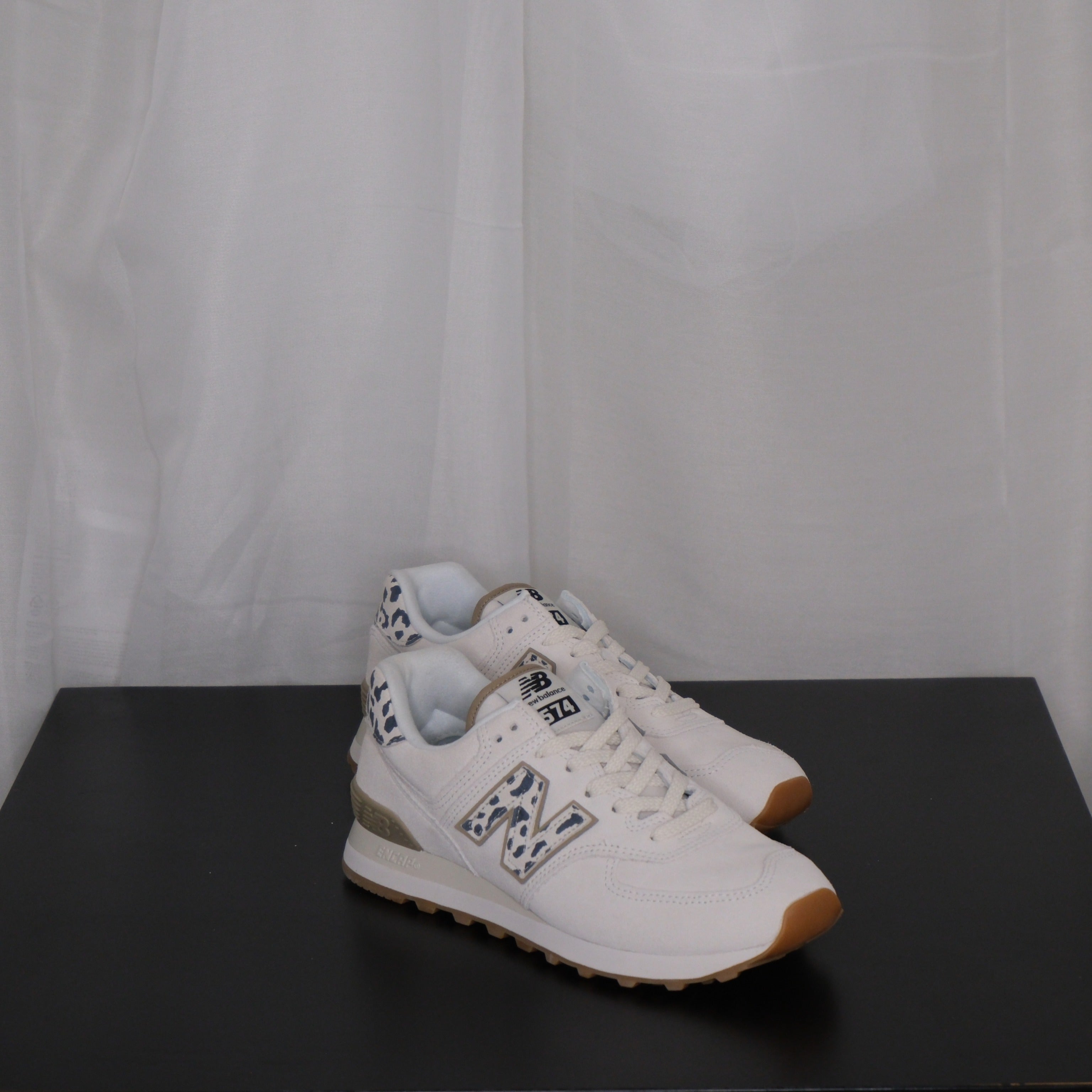 White sneakers with grey leopard design on a black surface and white sheer curtain background