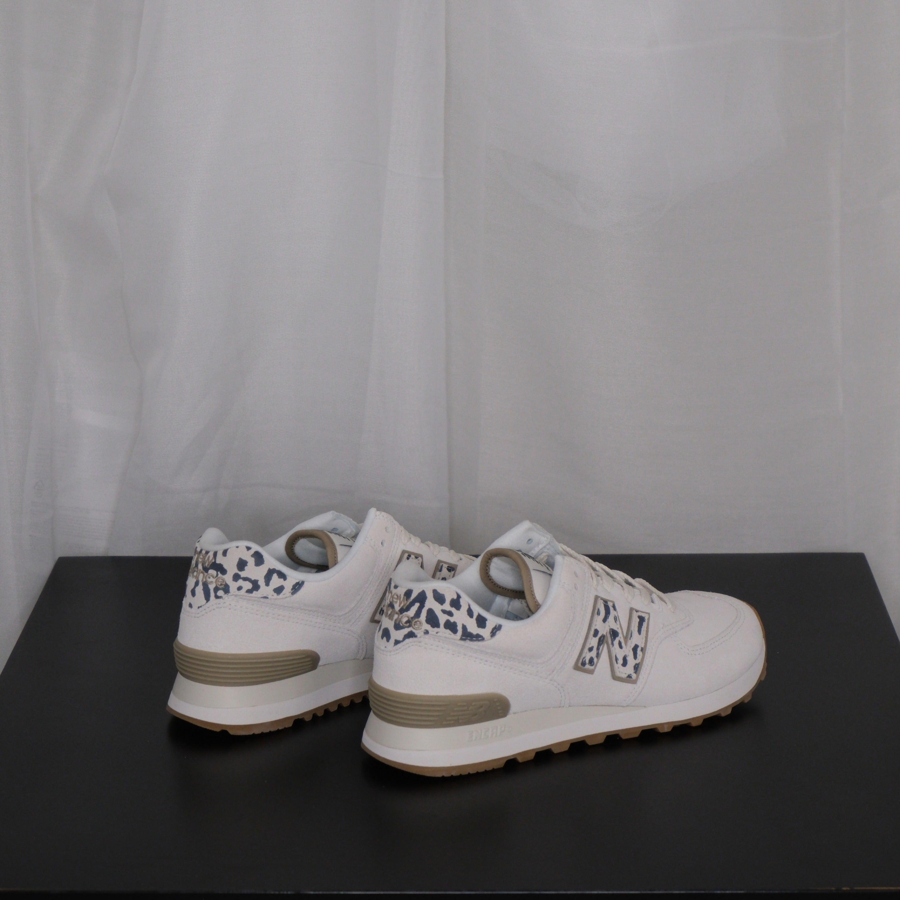 White sneakers with grey leopard design on a black surface and white sheer curtain background