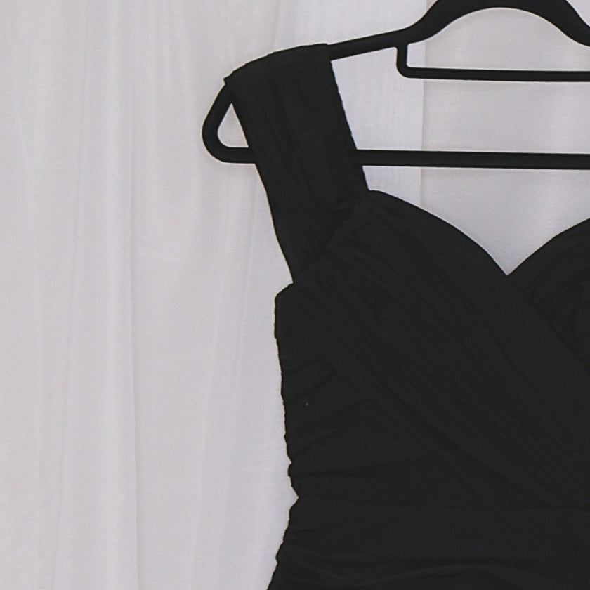 Black mini dress on a hanger against a white curtain background