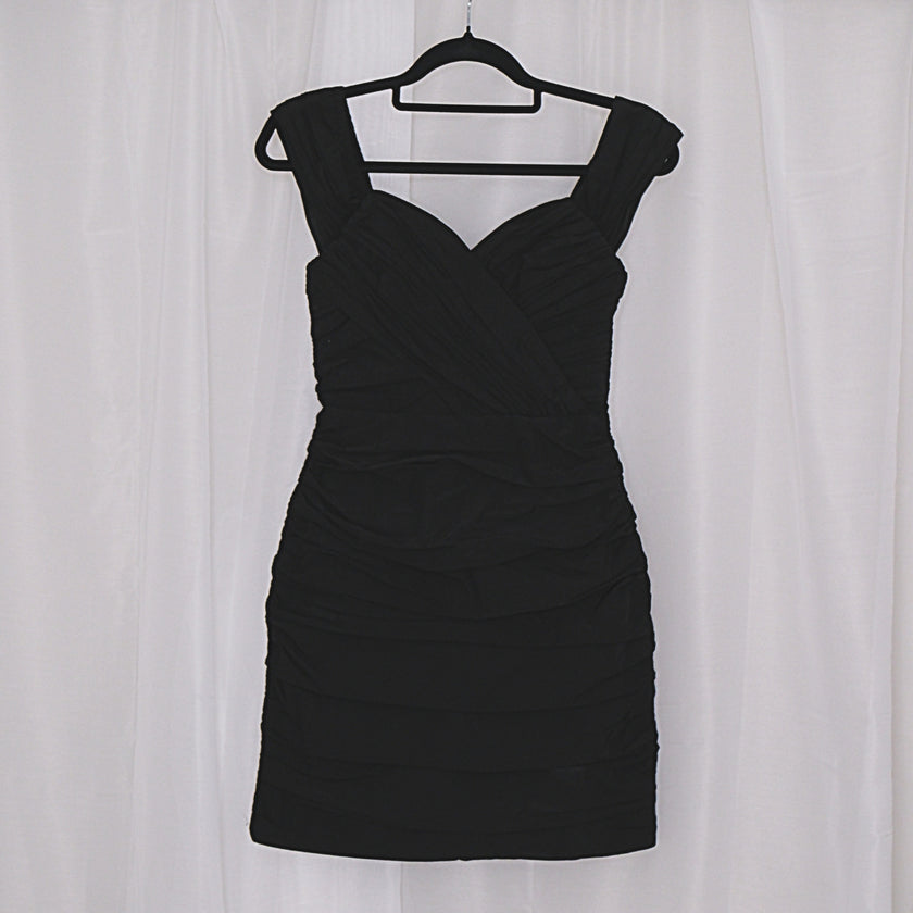 Black mini dress on a hanger against a white curtain background