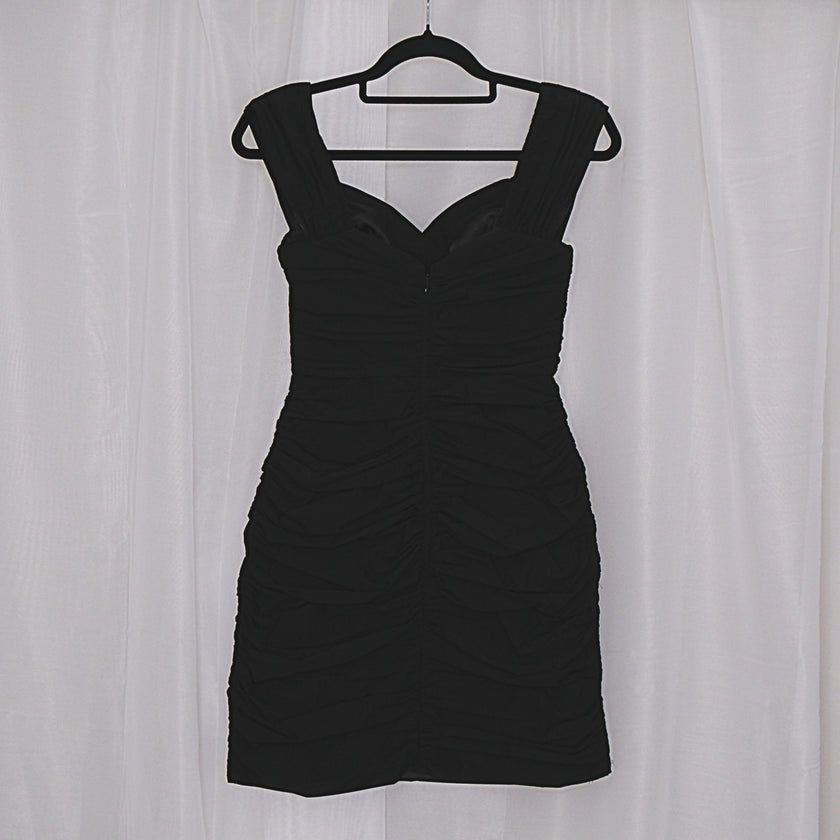 Black mini dress on a hanger against a white curtain background