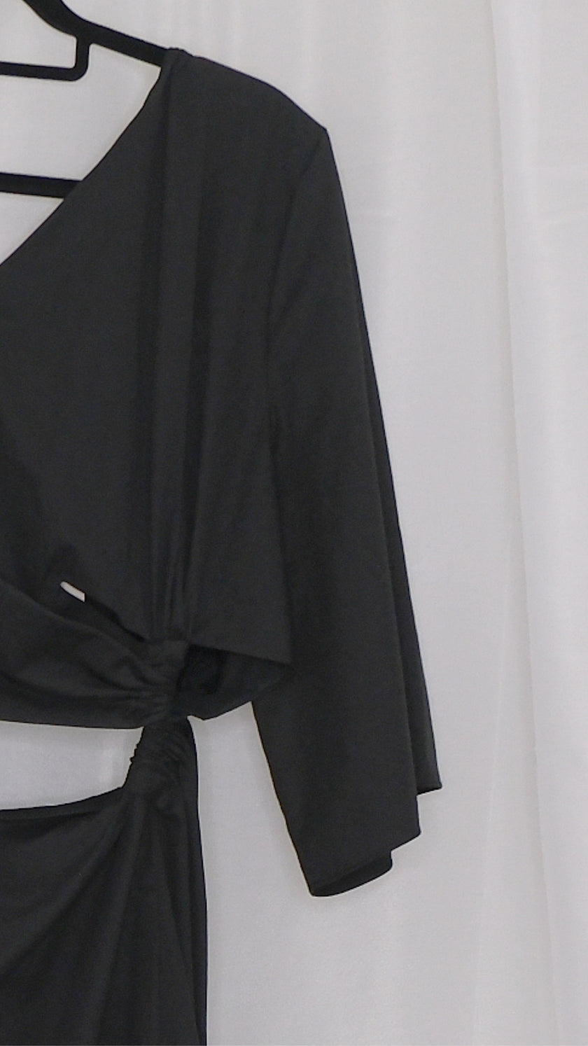 Black asymmetrical dress with cut outs on a hanger against a white background