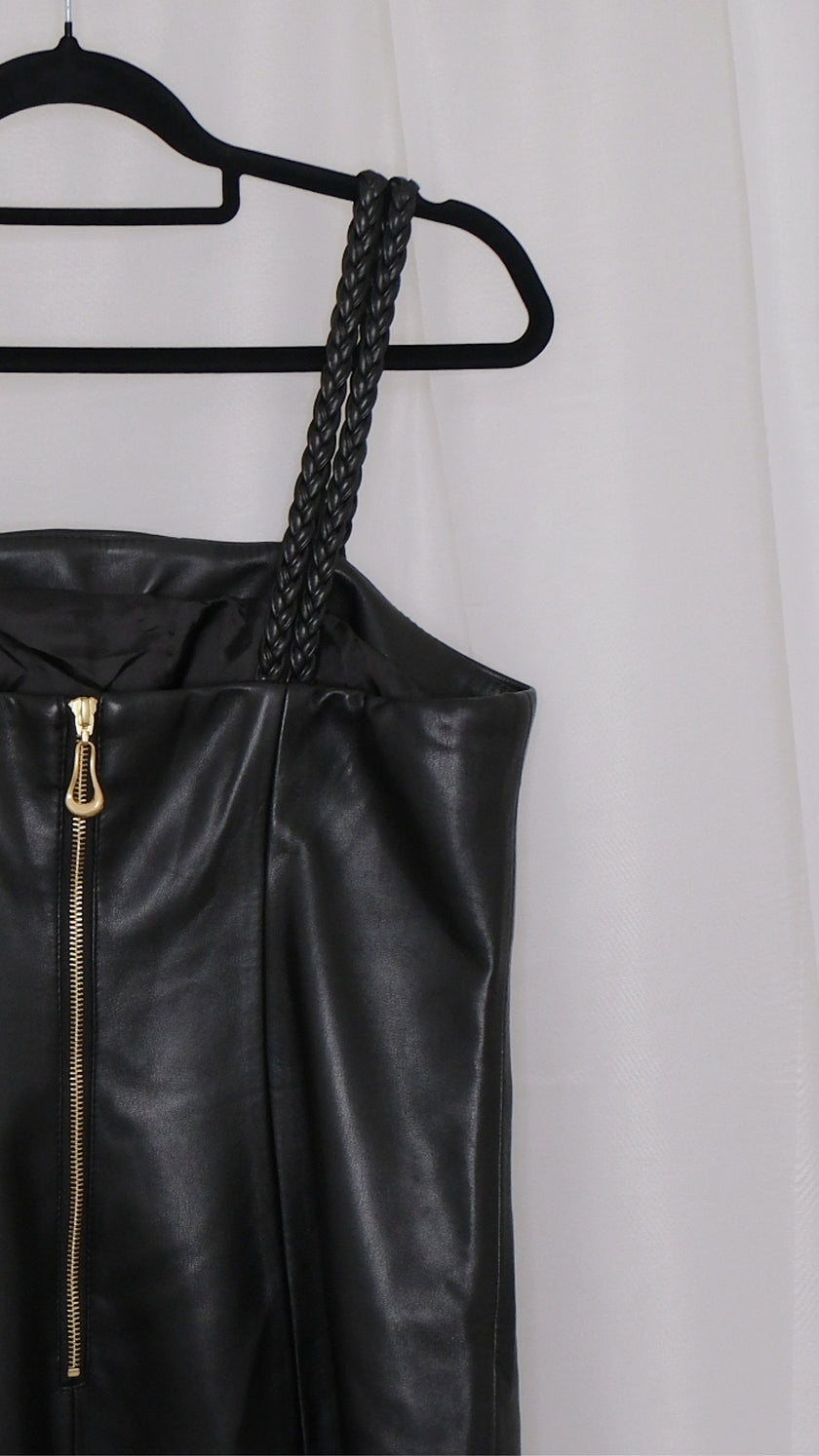 Black leather dress with braided straps on a hanger against a plain background
