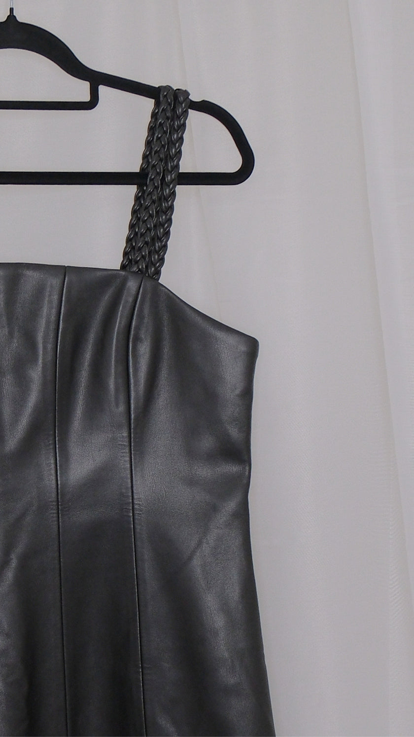 Black leather dress with braided straps on a hanger against a plain background