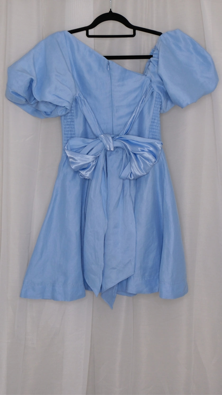 Light blue dress with puff sleeves and ties bow on a hanger against a white background
