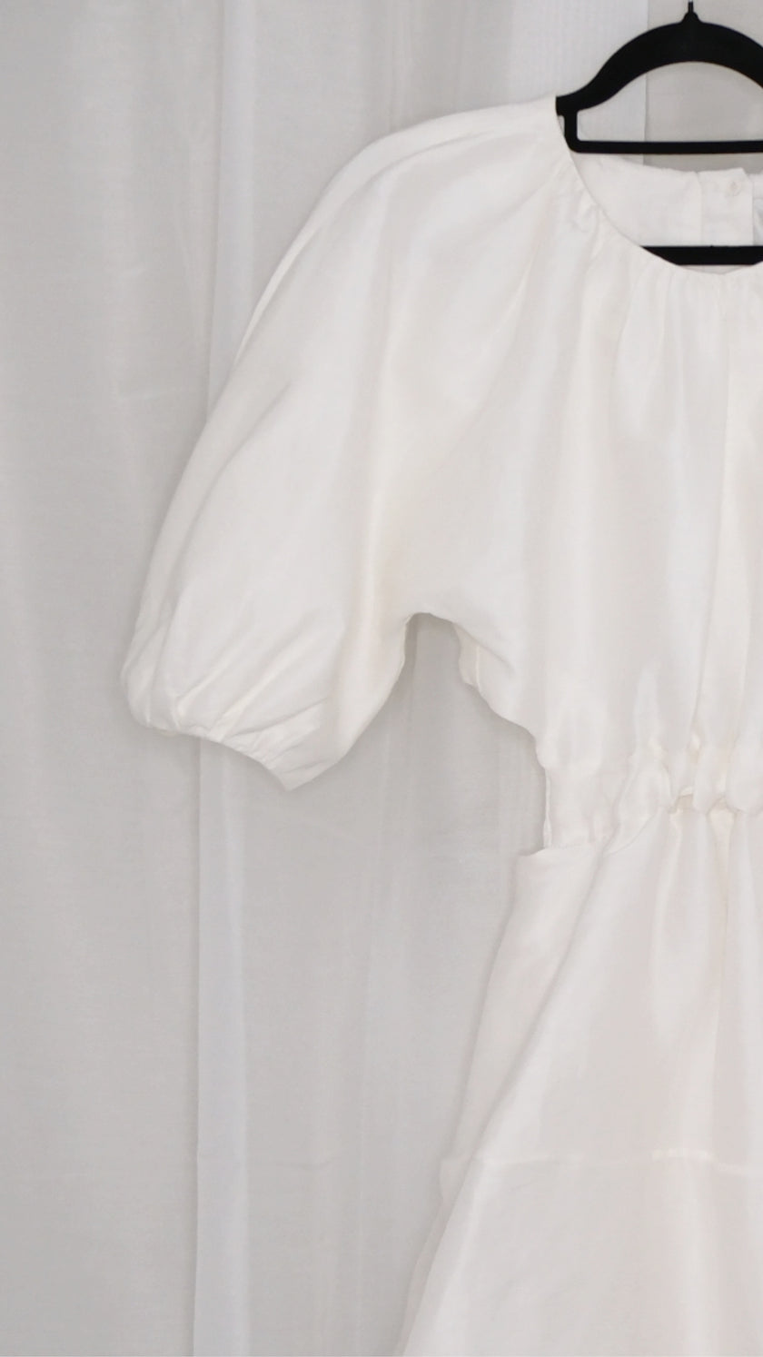 White dress with puff sleeves and tie waist on a hanger against a plain background