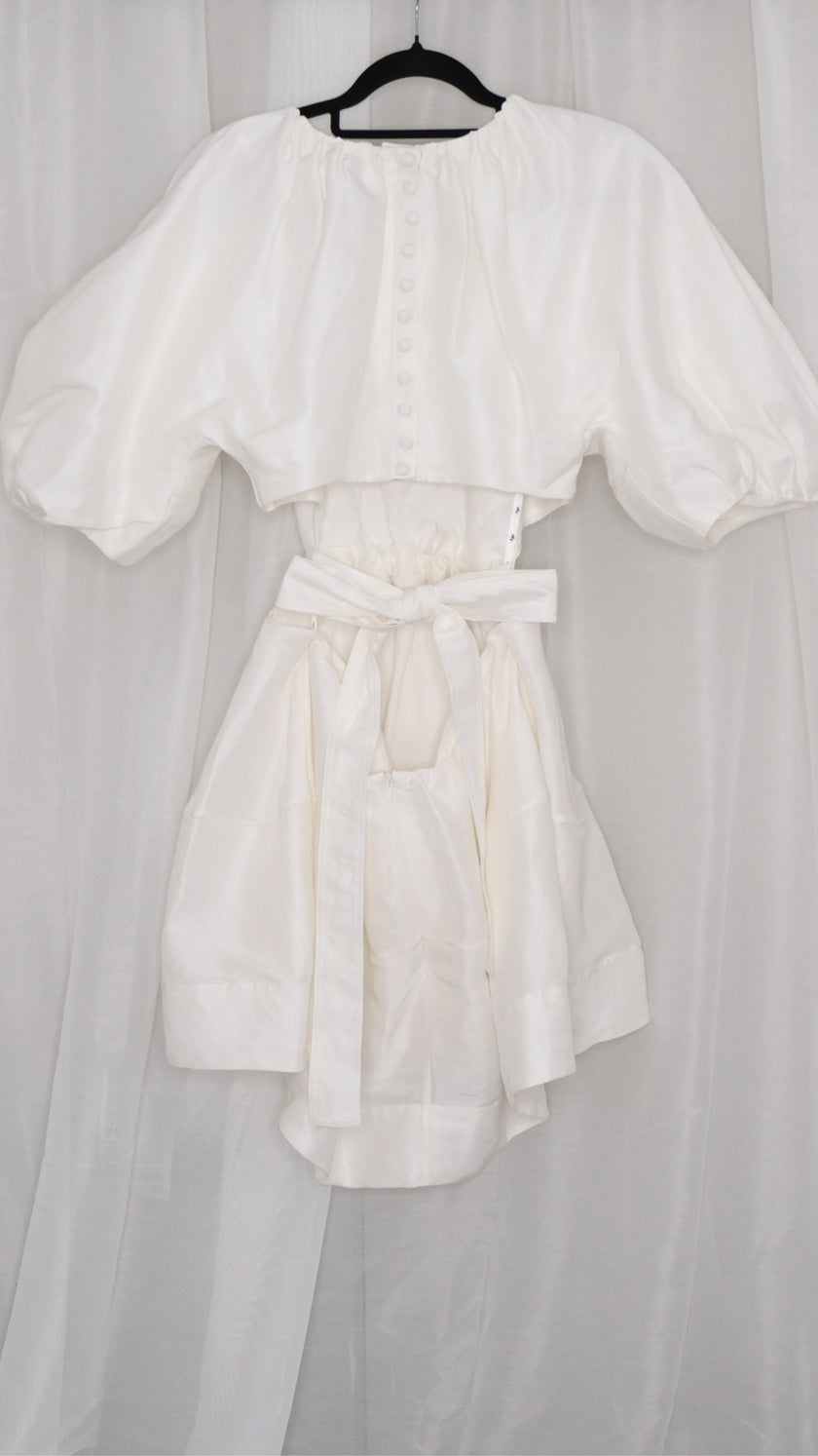 White dress with puff sleeves and tie waist on a hanger against a plain background