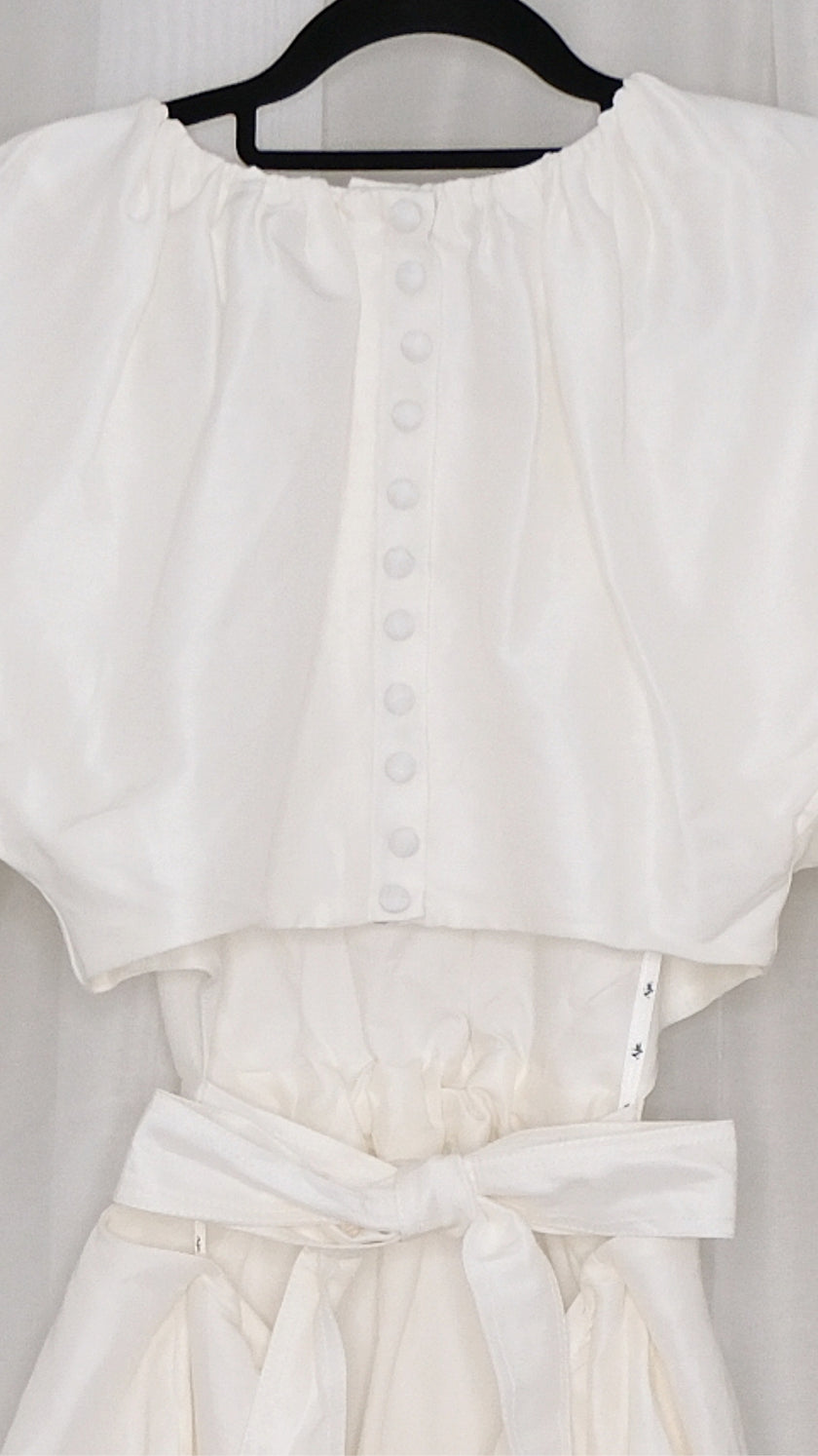 White dress with puff sleeves and tie waist on a hanger against a plain background