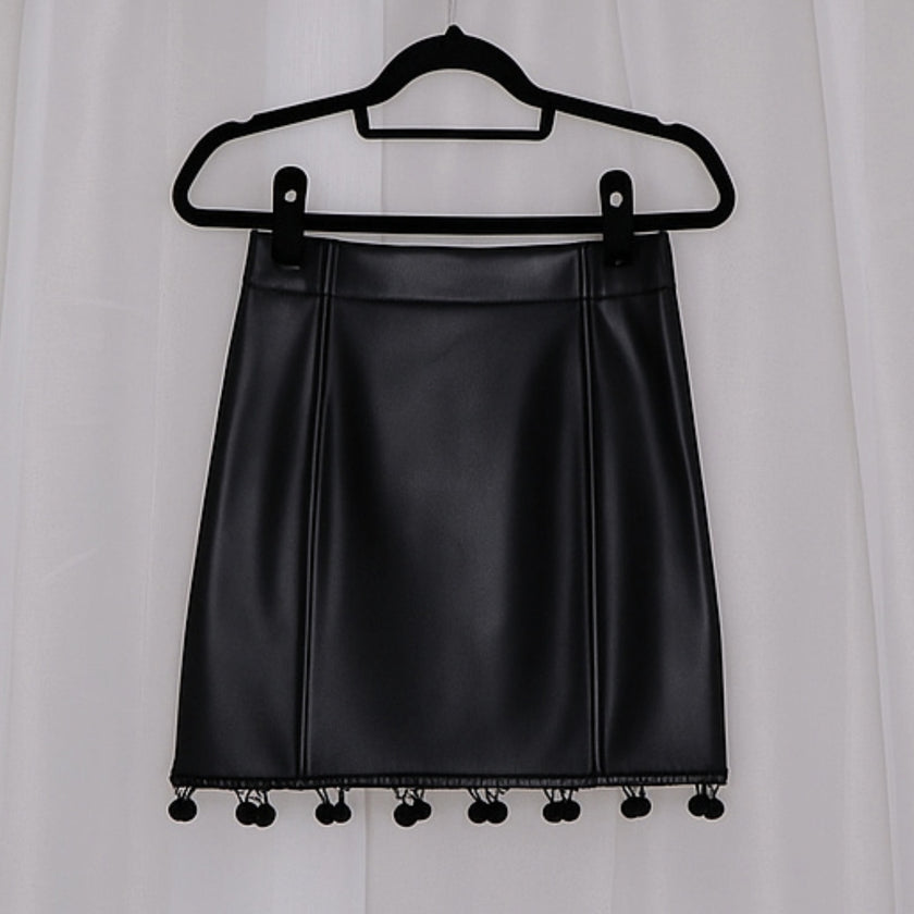 Black leather skirt with pom-pom details on a hanger against a white background