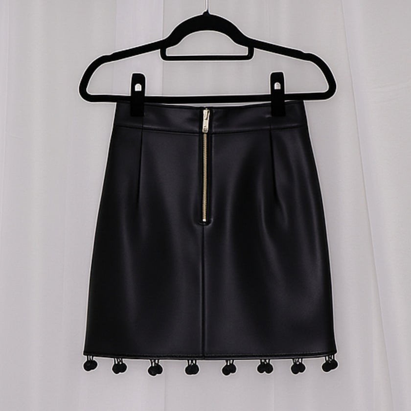 Black leather skirt with pom-pom details on a hanger against a white background