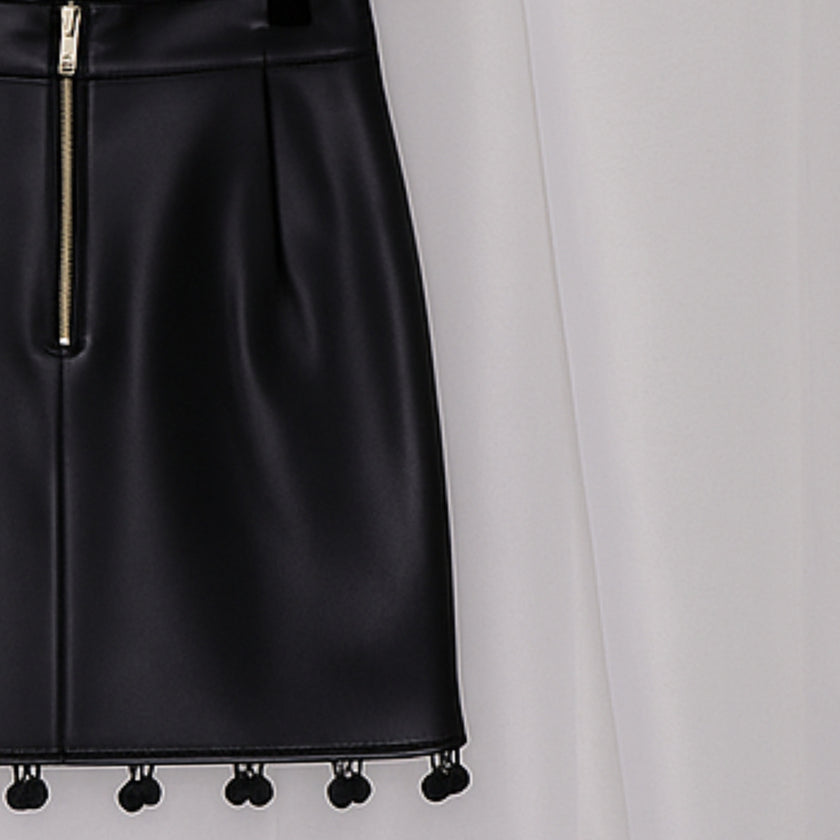 Black leather skirt with pom-pom details on a hanger against a white background
