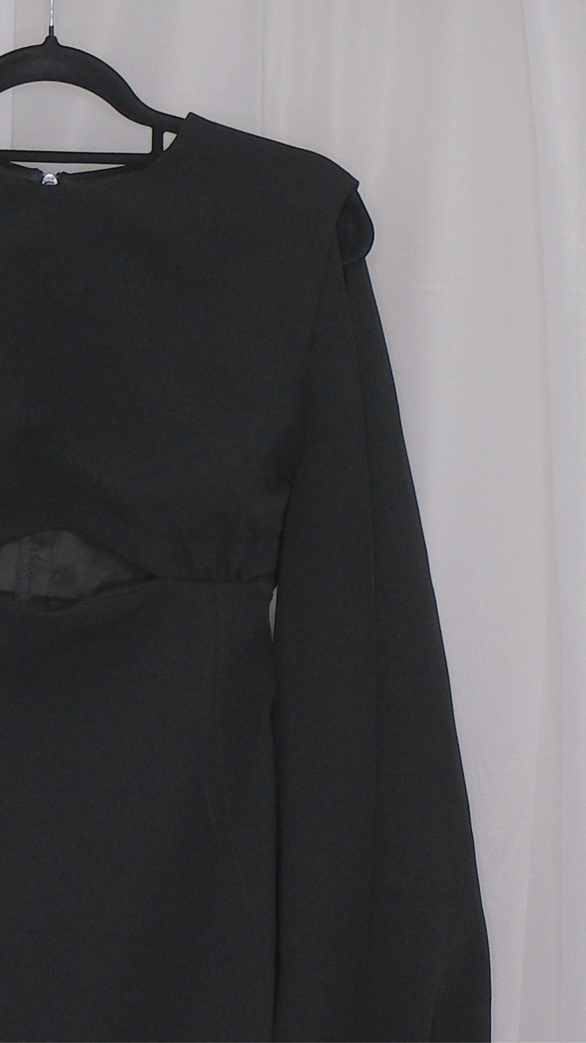 Black dress with long sleeves and cut outs on a hanger against a white background