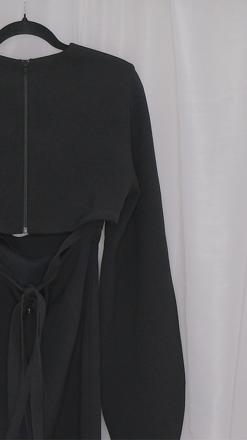 Black dress with long sleeves and cut outs on a hanger against a white background