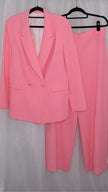 Pink suit with blazer and pants on hangers against a plain background