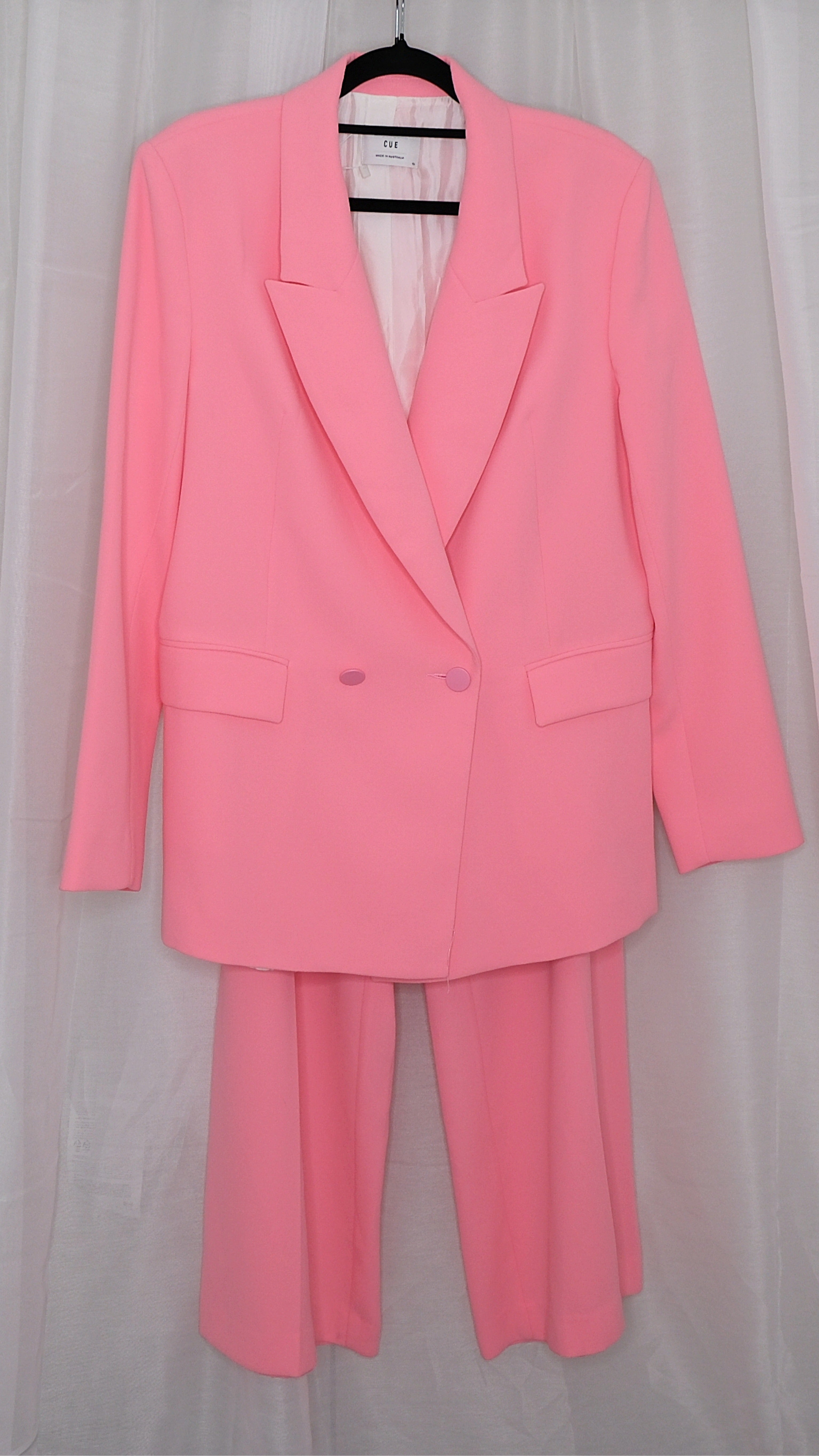 Pink suit with blazer and pants on hangers against a plain background