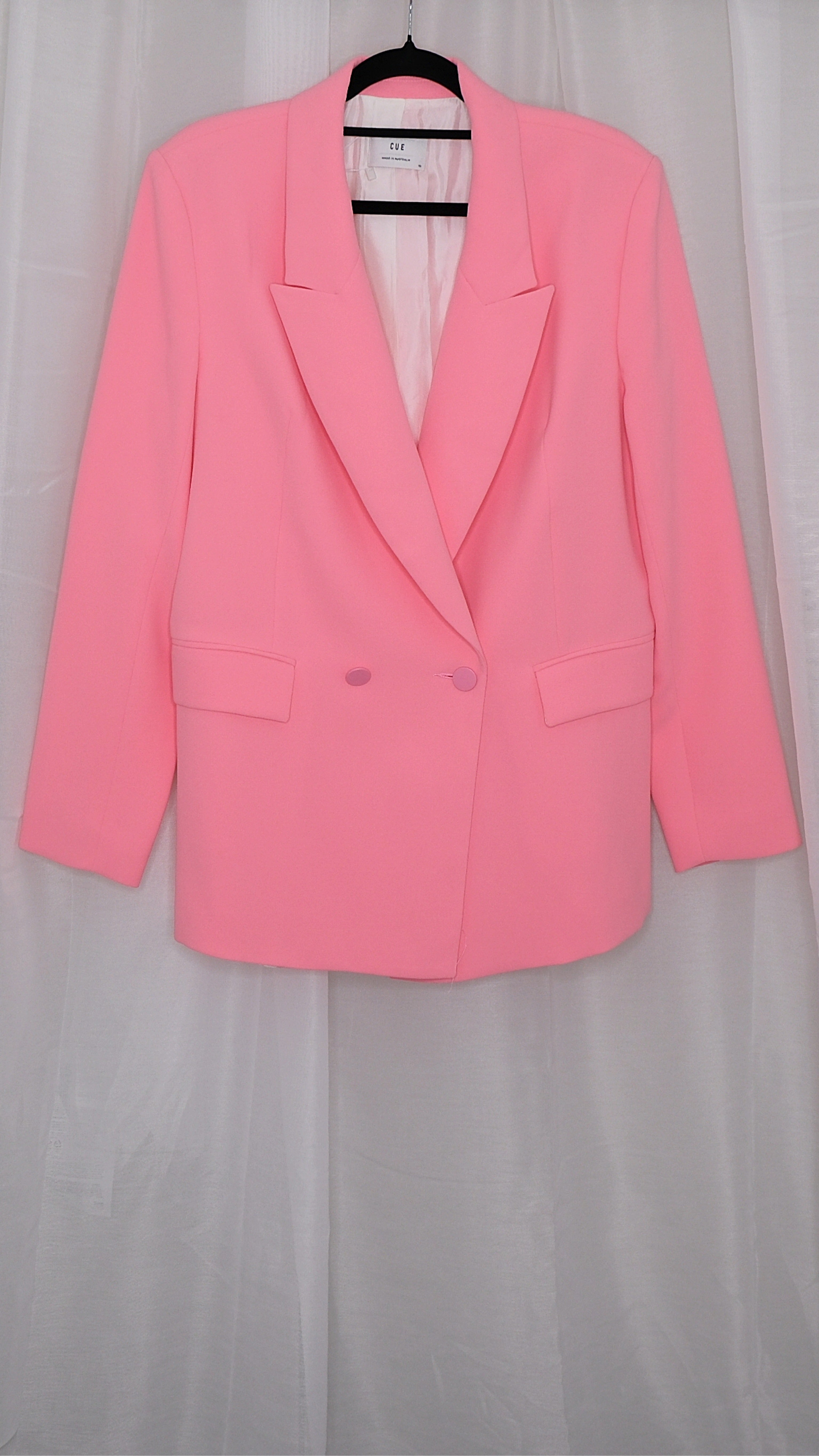 Pink suit with blazer and pants on hangers against a plain background