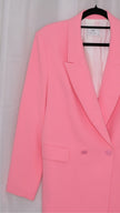 Pink suit with blazer and pants on hangers against a plain background