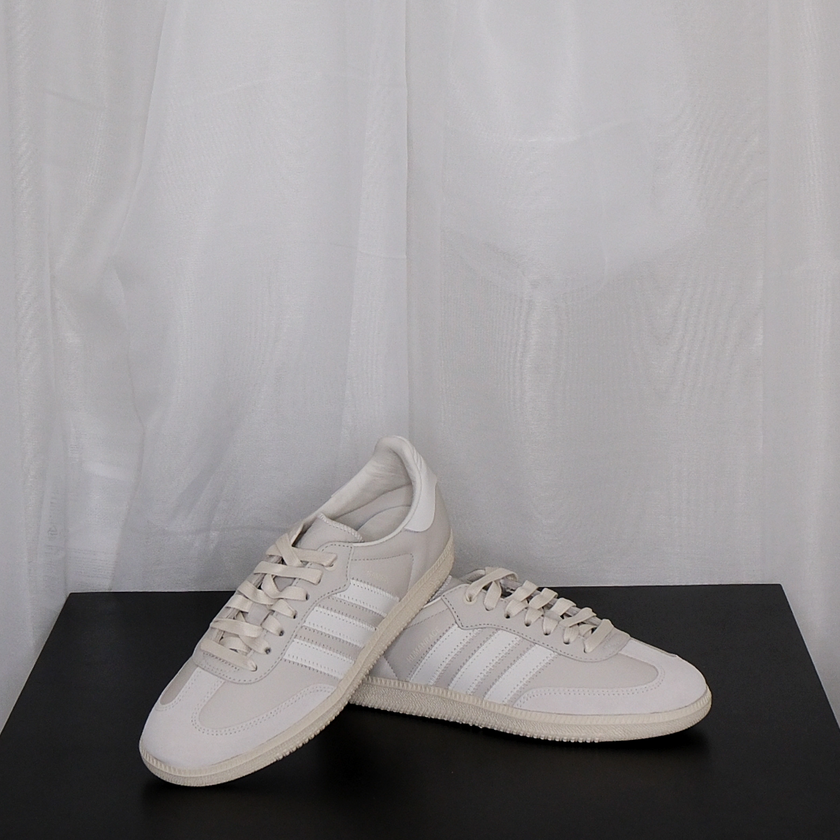 Pair of beige Adidas sneakers on a black surface with a white curtain background