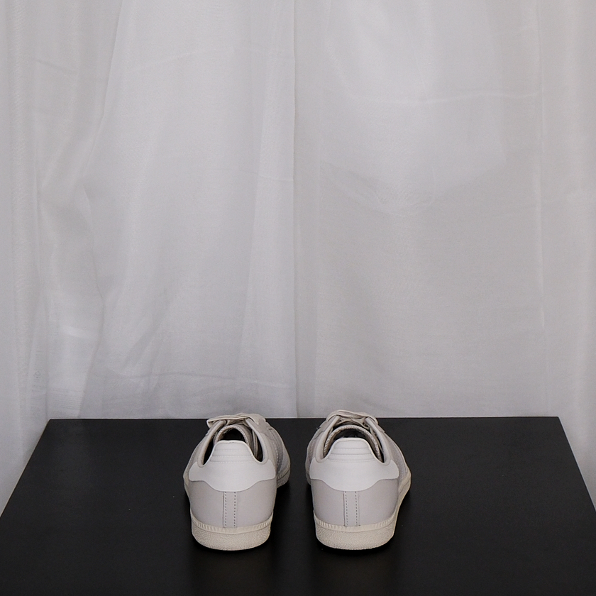 Pair of beige Adidas sneakers on a black surface with a white curtain background