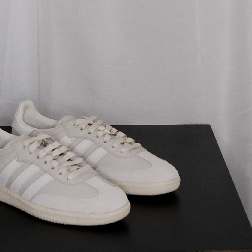 Pair of beige Adidas sneakers on a black surface with a white curtain background