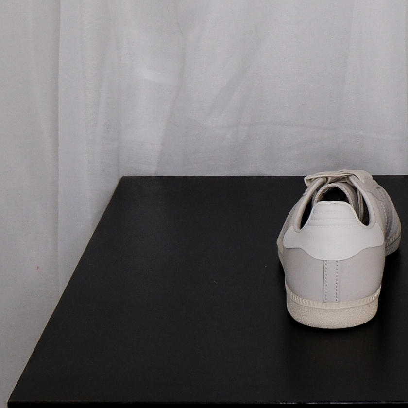Pair of beige Adidas sneakers on a black surface with a white curtain background


