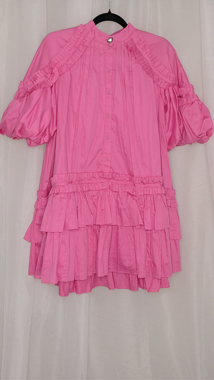 Pink dress with ruffled layers on a hanger against a plain background
