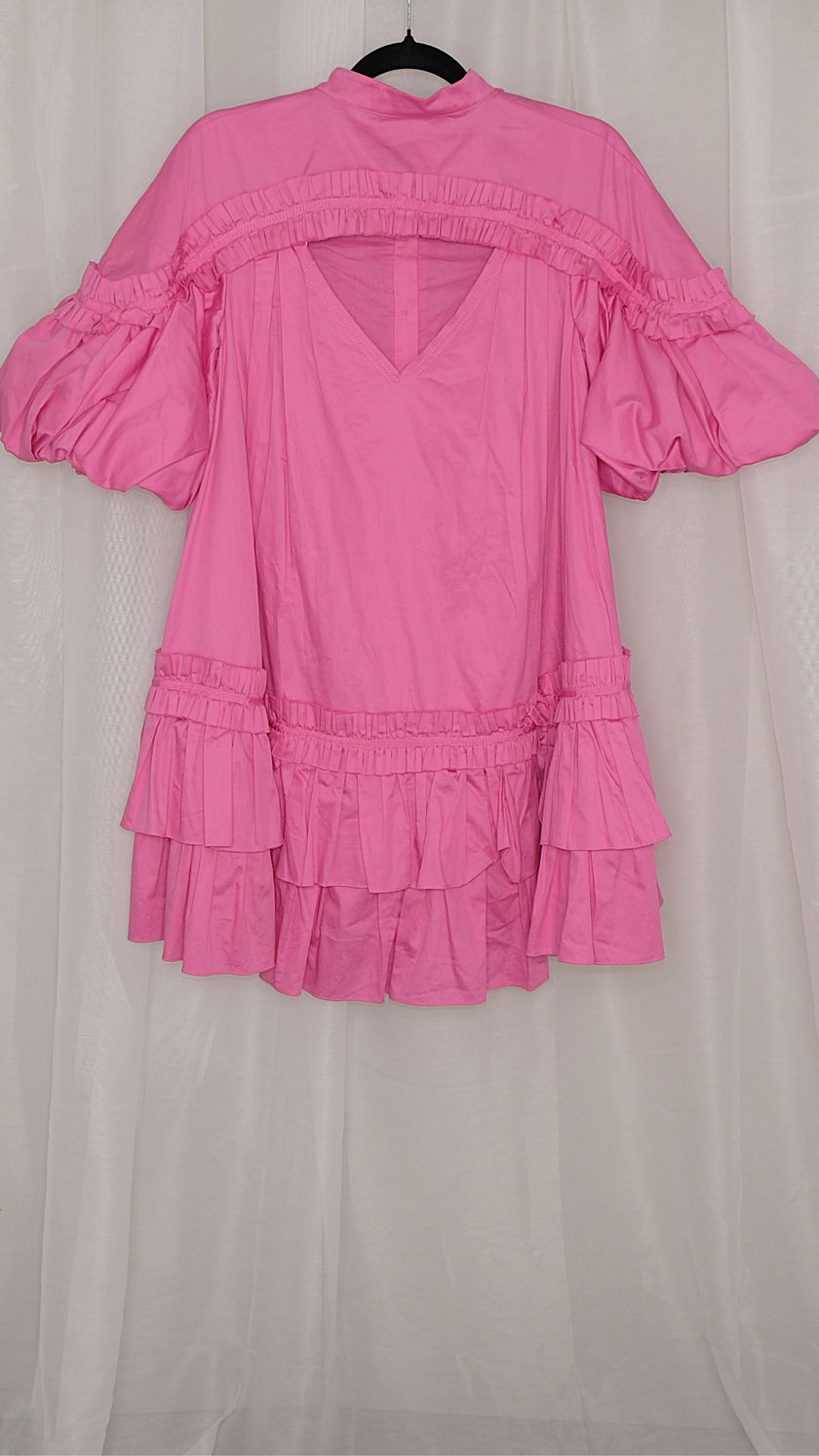 Pink dress with ruffled layers on a hanger against a plain background