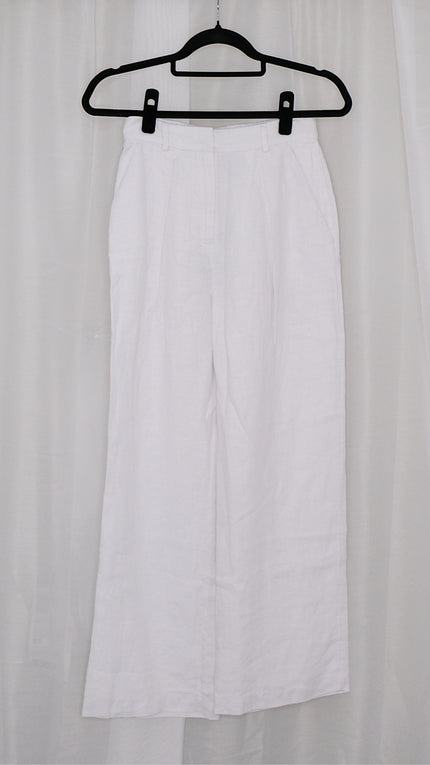 White wide leg pants on a black hanger against a white curtain background