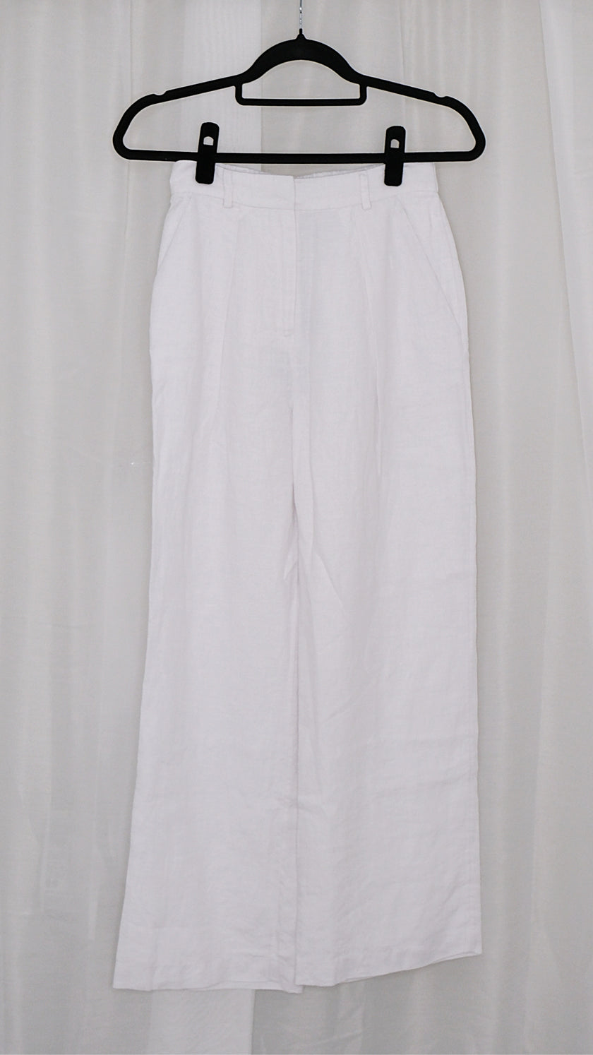 White wide leg pants on a black hanger against a white curtain background