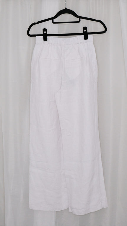 White wide leg pants on a black hanger against a white curtain background
