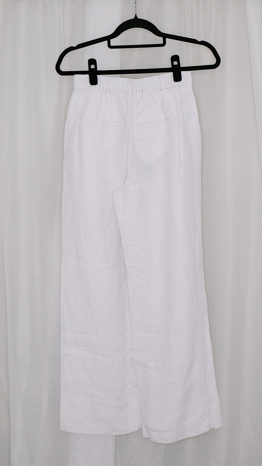 White wide leg pants on a black hanger against a white curtain background