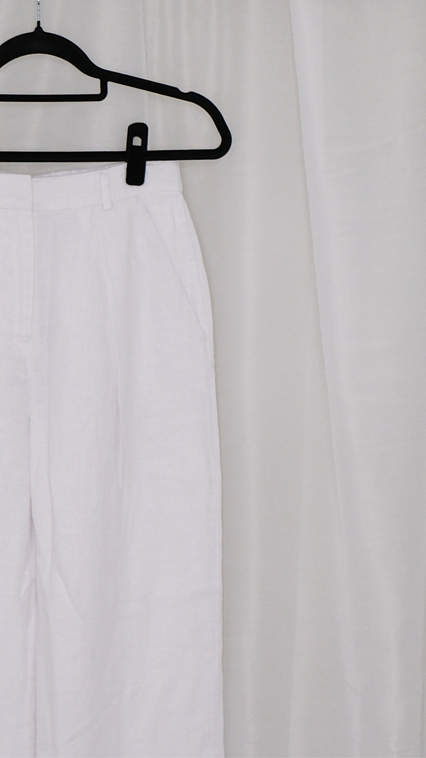 White wide leg pants on a black hanger against a white curtain background